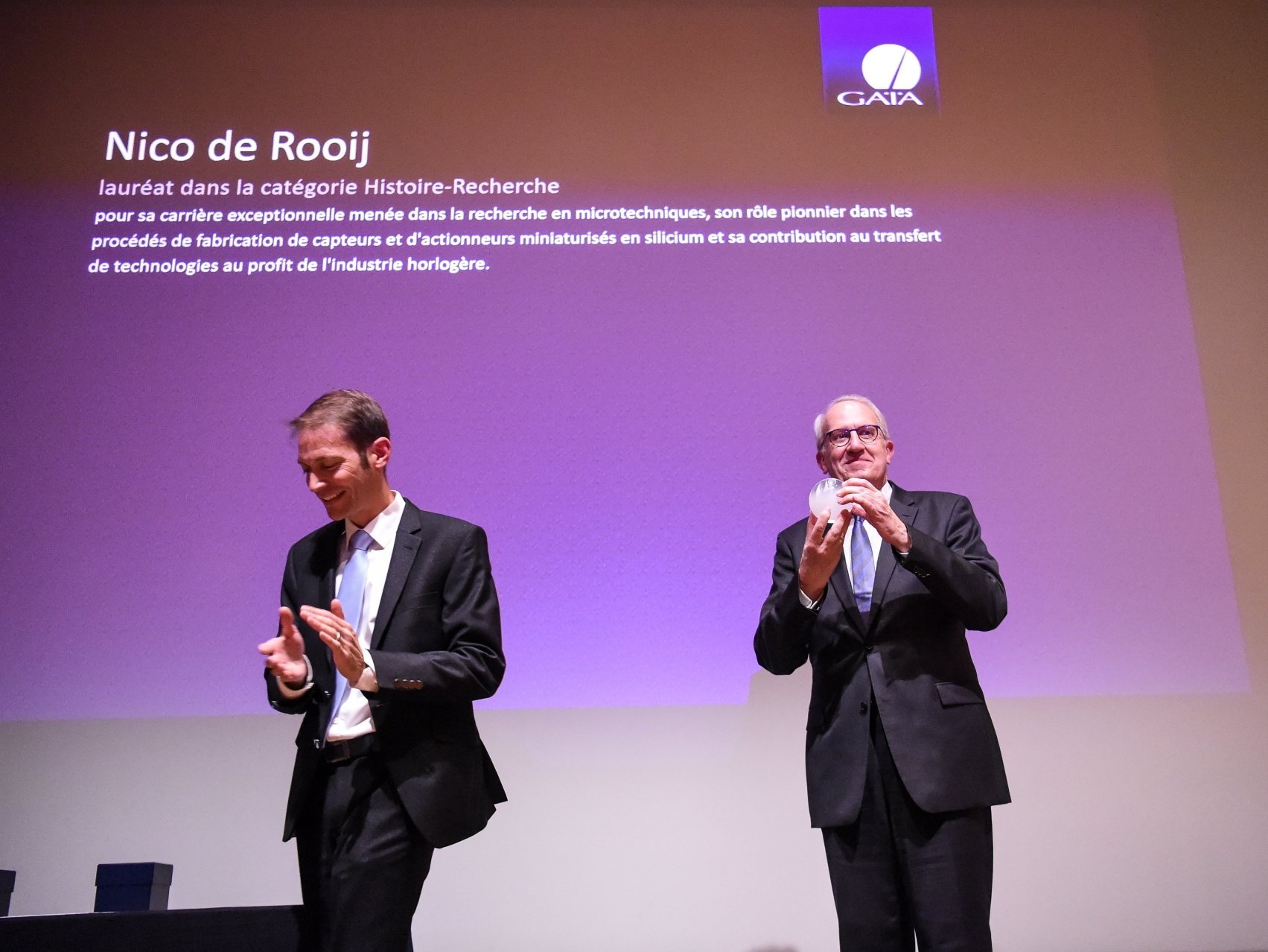 Le professeur Nico De Rooij (à droite, applaudi par le conservateur du MIH Régis Huguenin) a été récompensé pour sa contribution au transfert de technologies dans l'industrie horlogère.